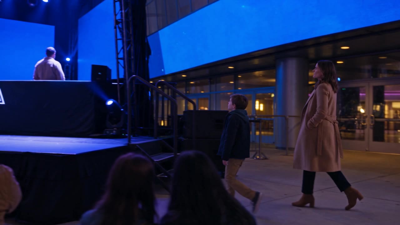 The boy and his mother come along the plaza toward the stage